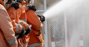 image shows a line of firefighters holding a spraying hose